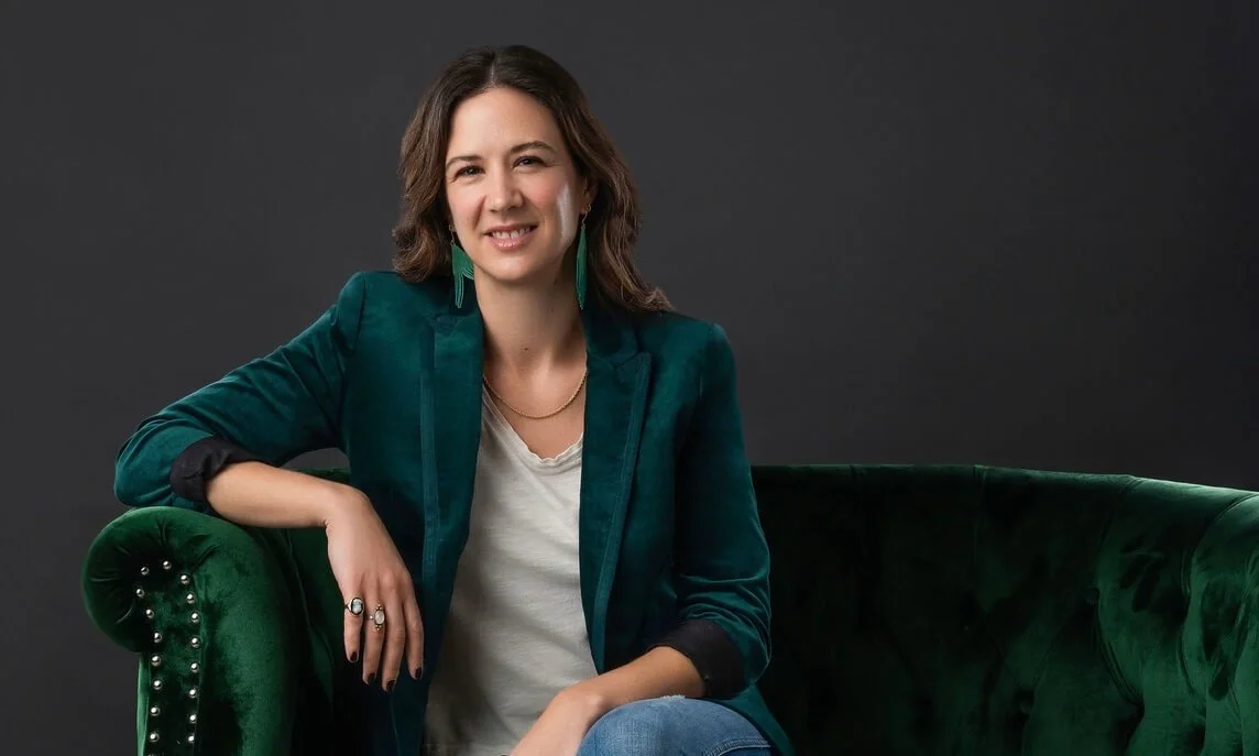 Genevieve Camp sitting on a green velvet couch wearing a green velvet blazer and white shirt.
