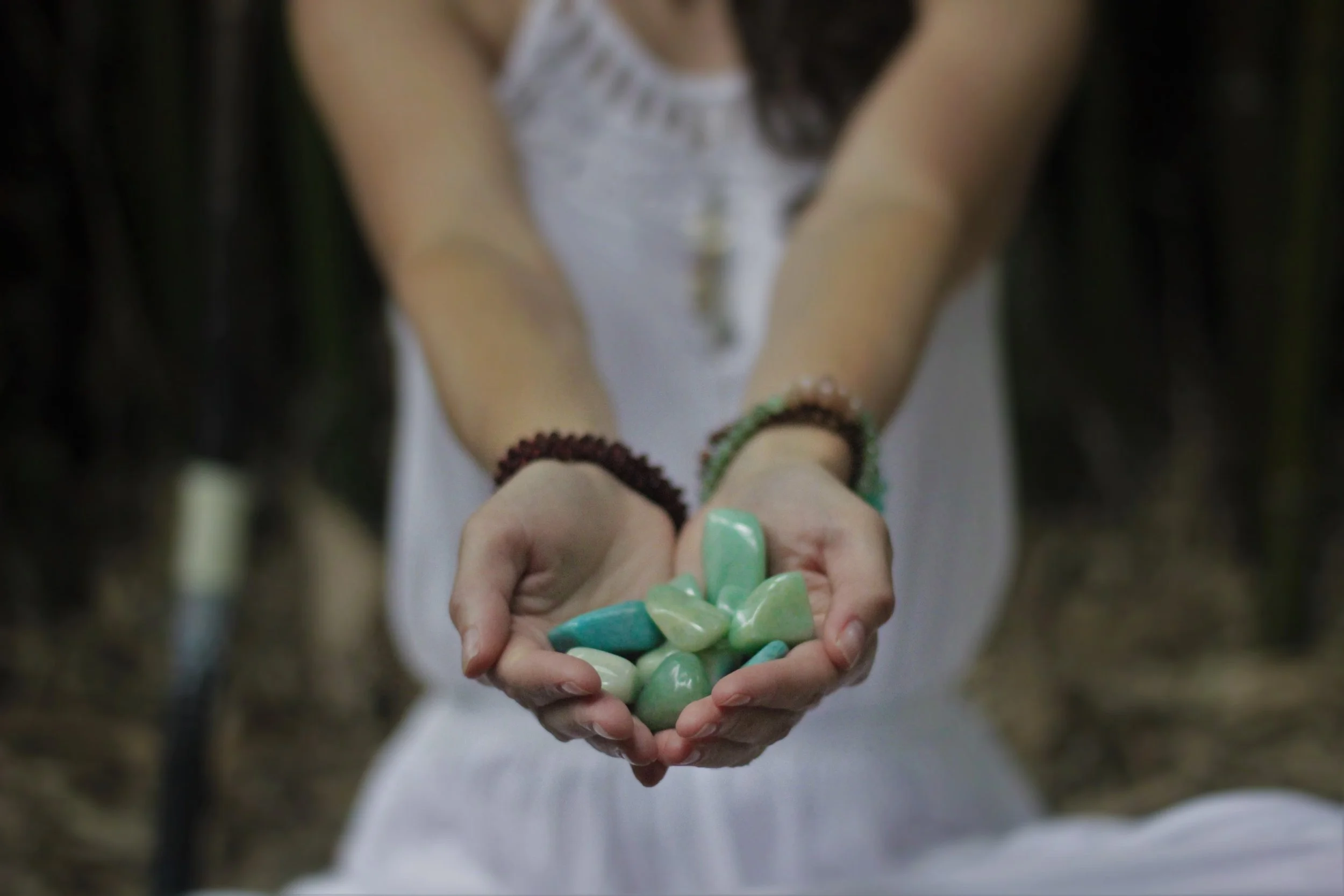Close up of a woman's outstretched hands holding several polished green aventurine stones.