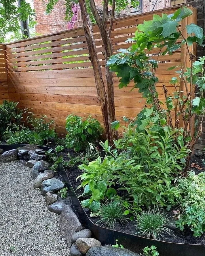 Custom fencing, gravel, and garden beds lined with large stones