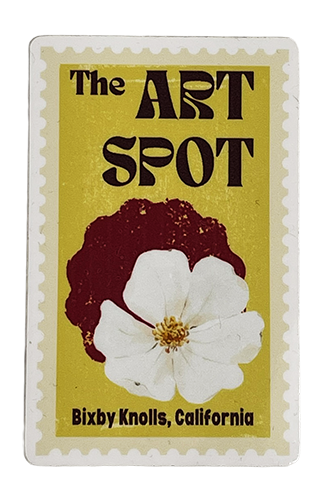 A yellow poster with black text that reads "The Art Spot" and mentions Bixby Knolls, California. It features a silhouette of a person's head with curly hair, positioned behind a white flower.