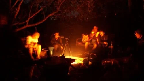 Group of people sitting around a campfire at night