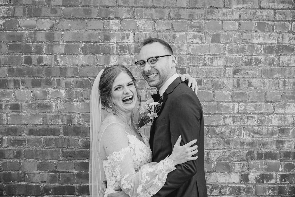 Bride laughing with groom at brick wall