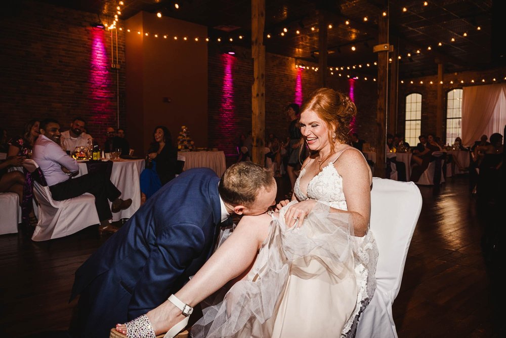 Groom removes garter with teeth from laughing brides leg