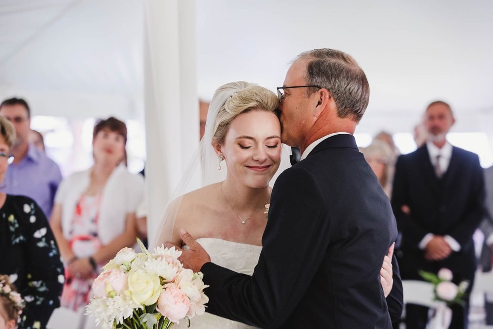 Father kisses bride at farm wedding ceremony
