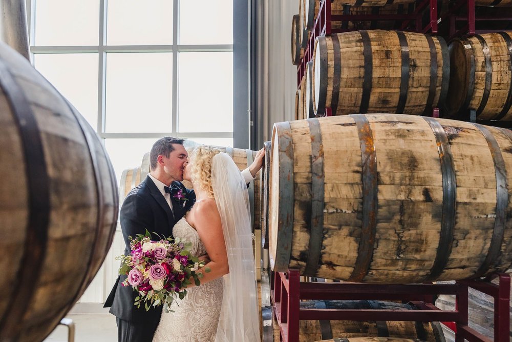 Bride and groom kiss with barrels at Destihl Brewery