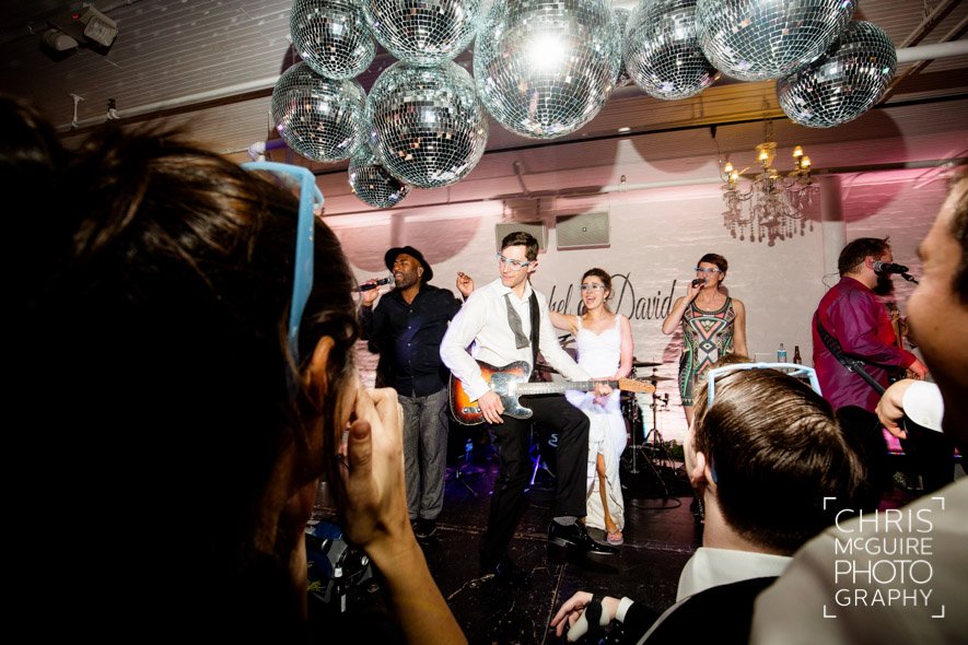 groom playing guitar with live band at wedding reception