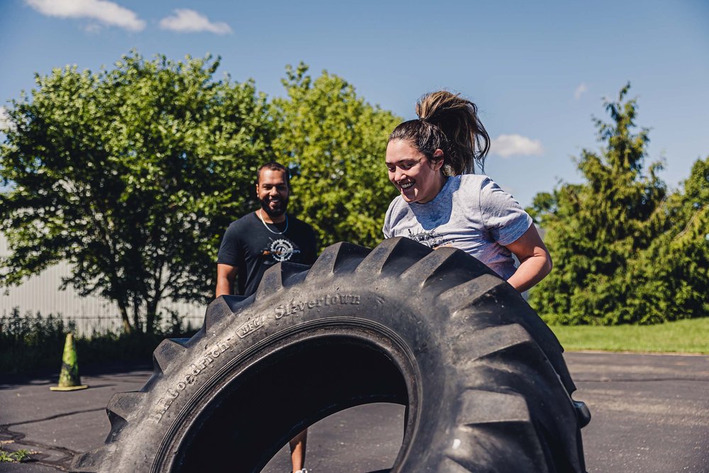 Young woman lifting tire with coach