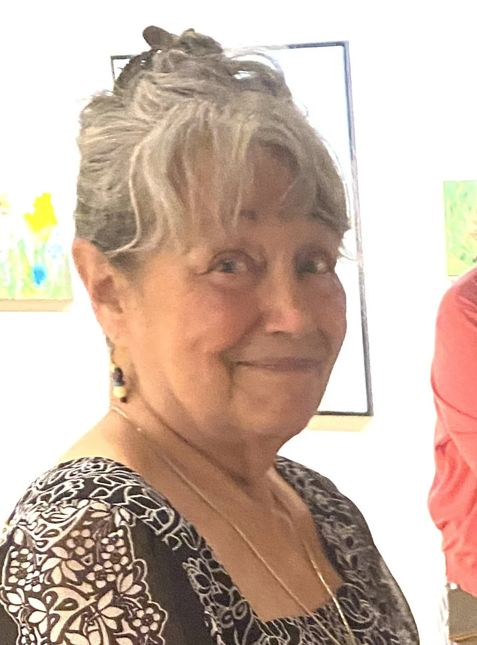Smiling lady with her salt and pepper hair pulled up. She's wearing a black and white floral blouse.
