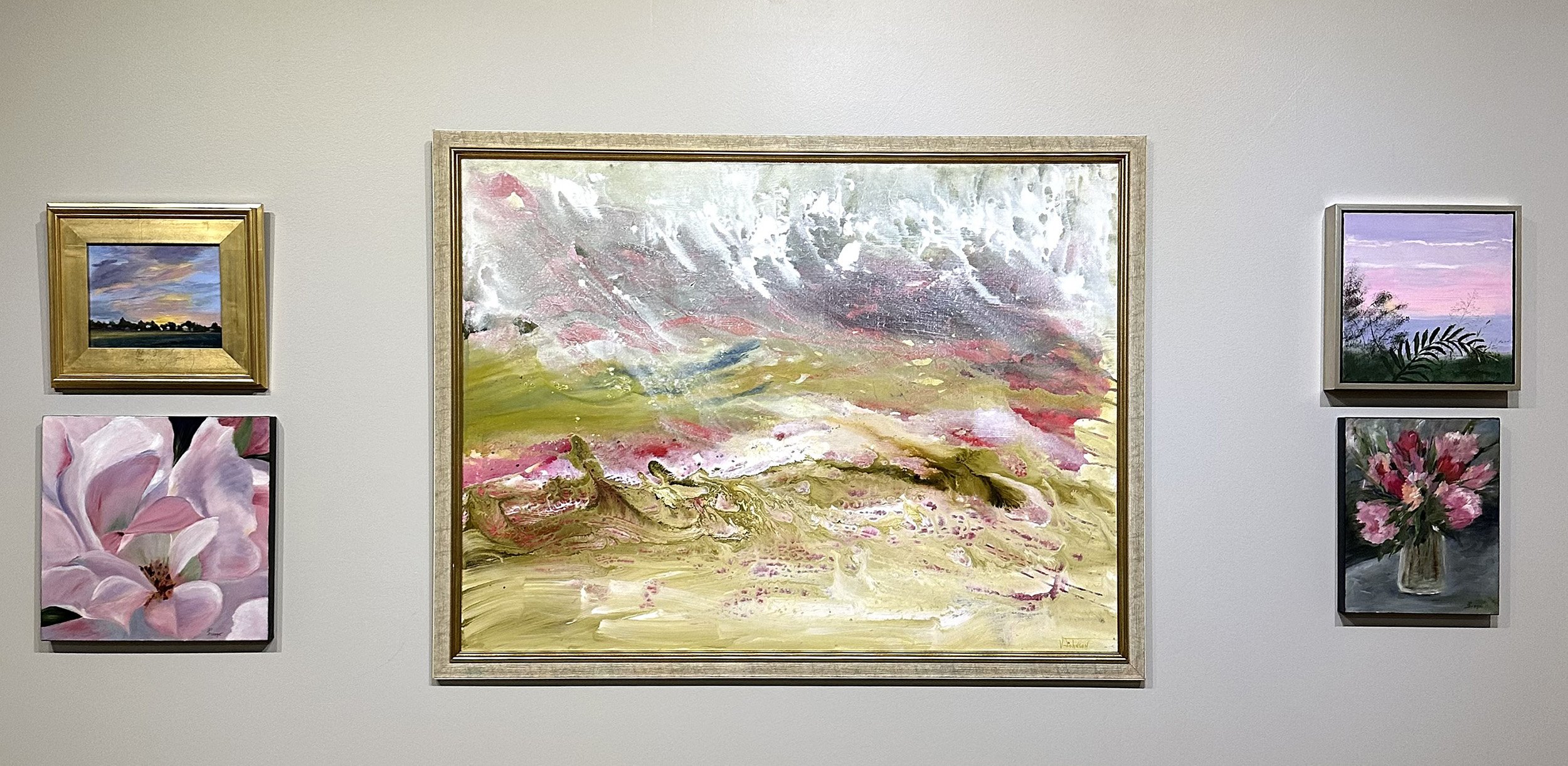 Grouping of 5 paintings hanging on the wall in an art gallery. Four small ones include two landscapes and two floral pieces. In the center is a large abstract painting. All 5 pieces feature pink hues.