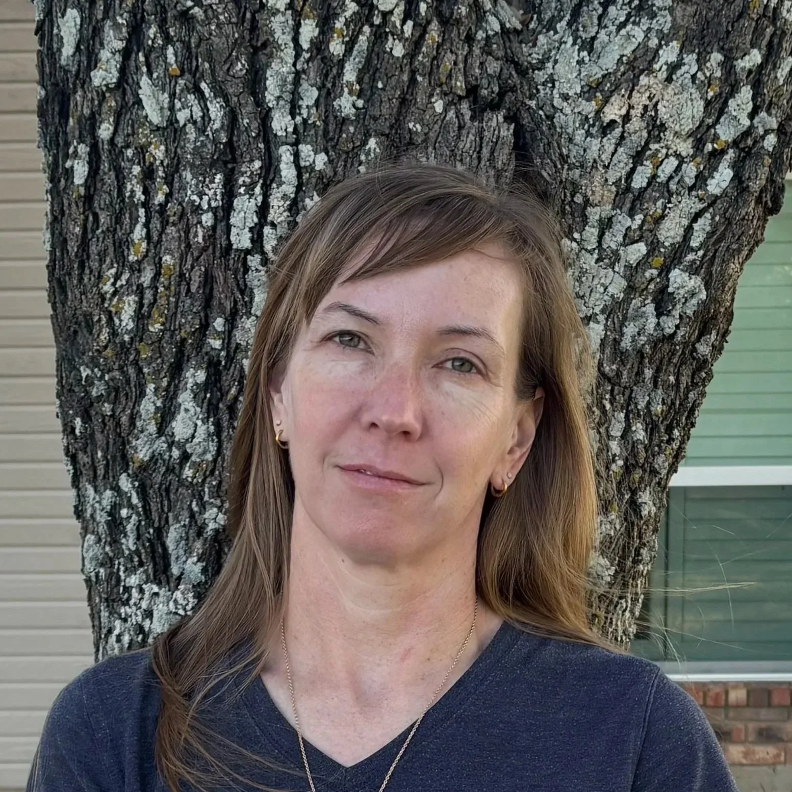 Christine in a blue shirt in front of a tree