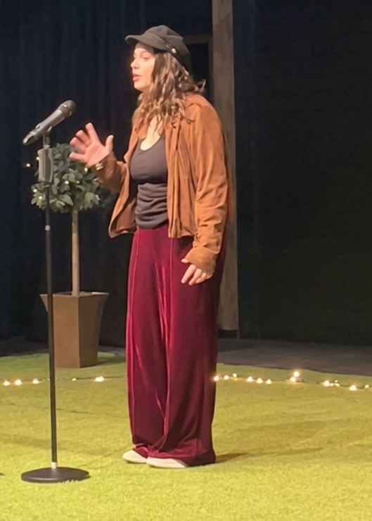 Blossom, a white, brunette woman, performing a poem on stage