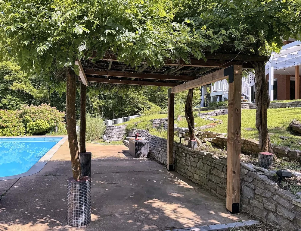 Reinforced poolside pergola with new square cedar posts and beams and black steel corner brackets under a vine canopy