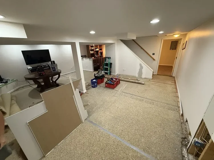 Basement renovation in progress with tools, drywall, and a table. Stairs and wall repairs visible