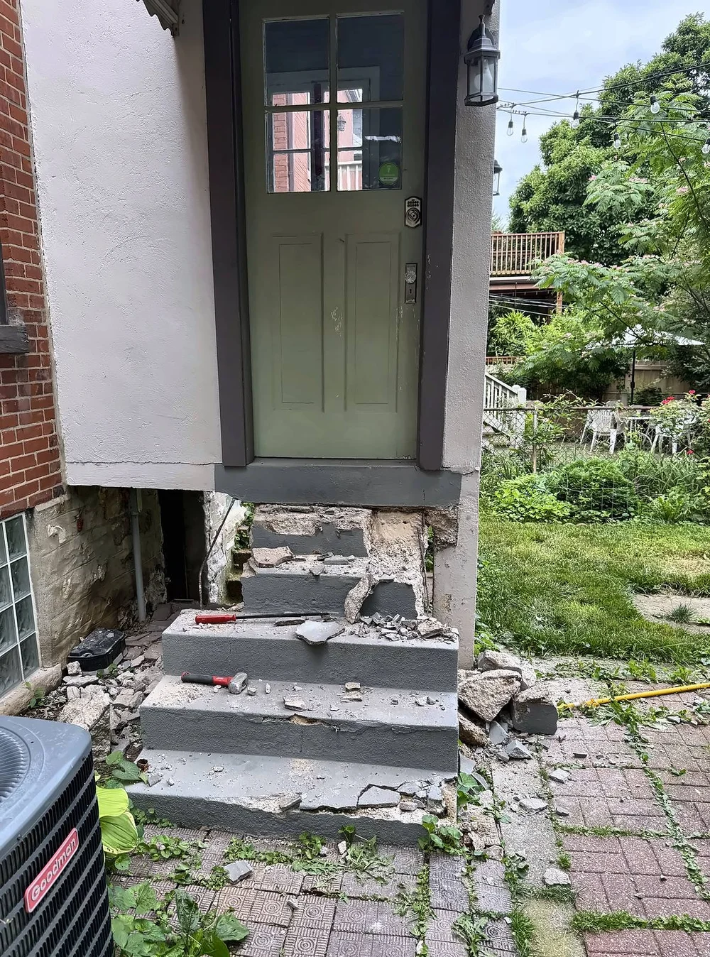 Demolition in progress: old concrete back steps partly broken out, with a hammer and chisel on the steps