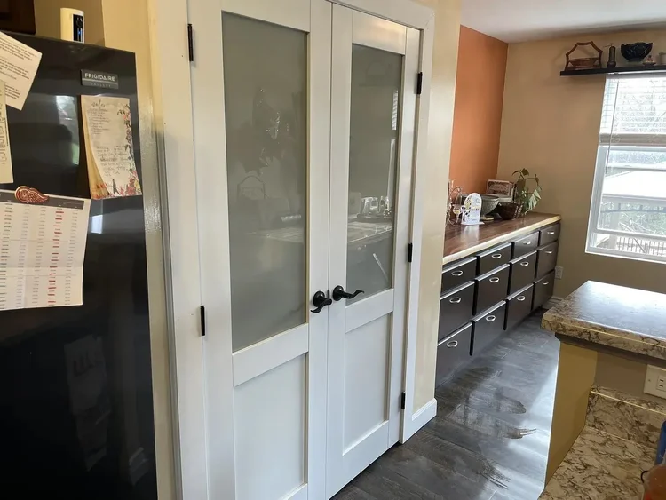 Kitchen with double pantry doors, fridge with notes, wooden counter, orange wall, and large window