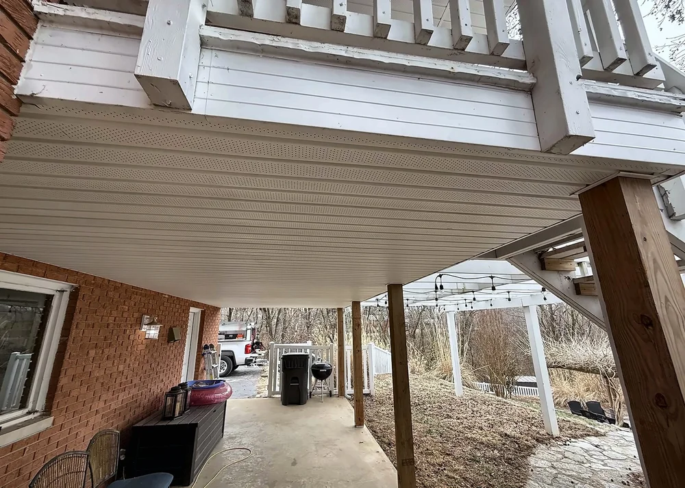 View under the deck toward the driveway, showing the new vinyl soffit ceiling and wood support posts
