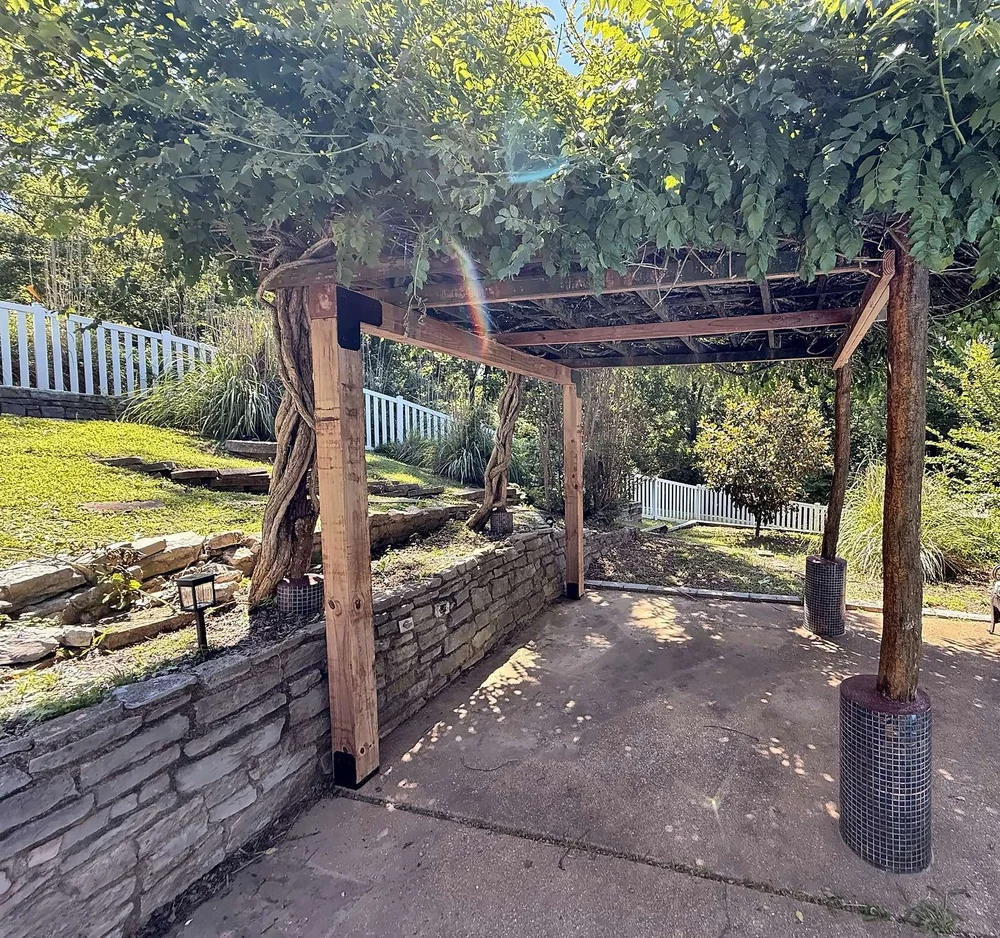 Wide view under the reinforced arbor showing new cedar posts and beams beside the original round posts on tiled bases