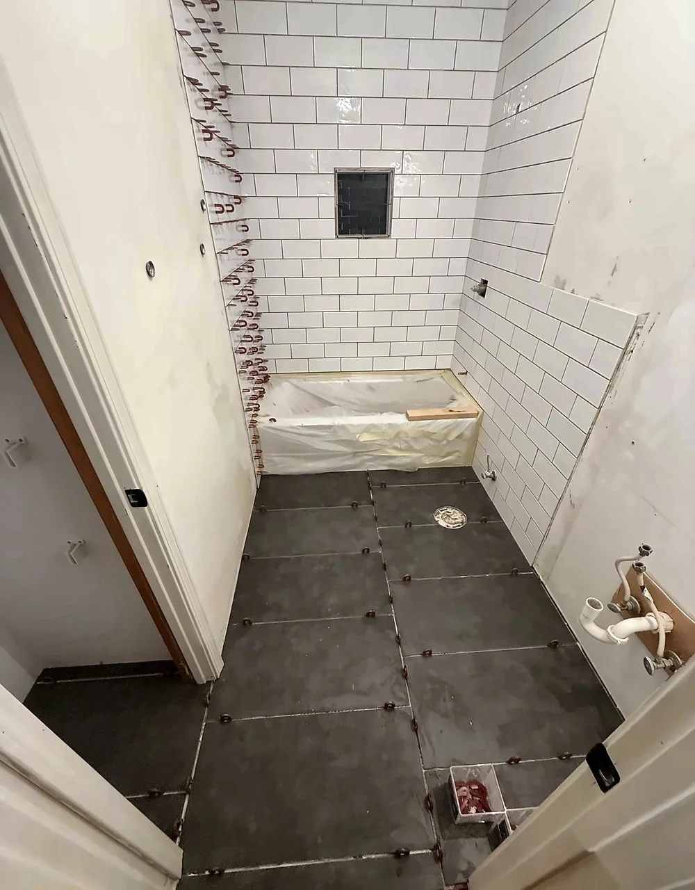 White subway tile going up around the tub with spacers, and large dark floor tile set with leveling clips