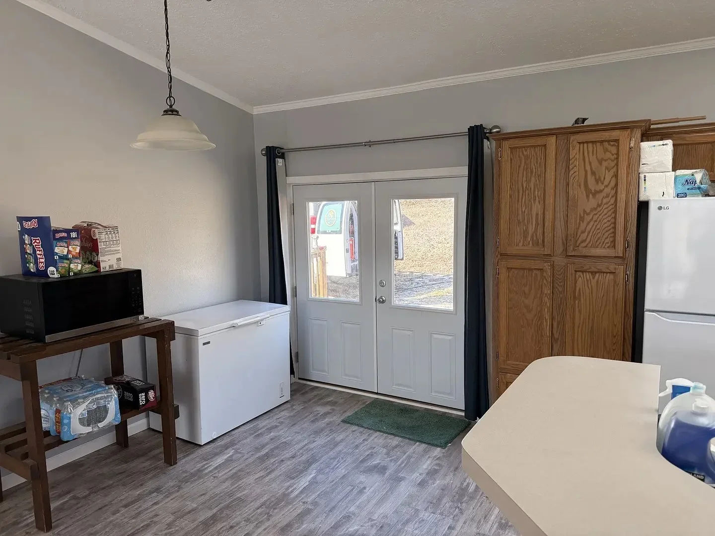 Kitchen area with a white freezer, microwave on a wooden stand, and wooden cabinets near glass doors