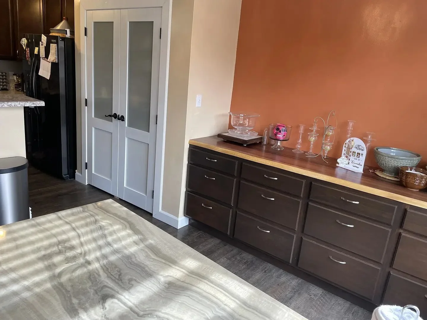Kitchen with dark wood cabinets, orange accent wall, and glass decor on counter