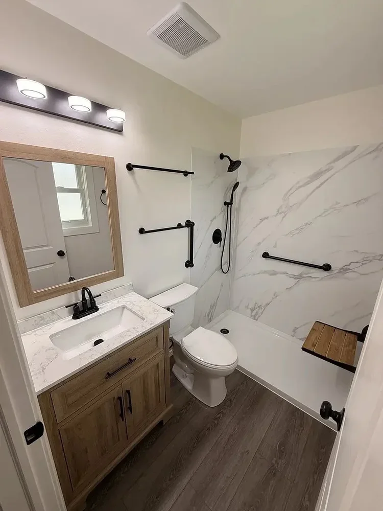Modern bathroom with wood vanity, marble countertop, shower with grab bars, and fold-down seat. Wood floor