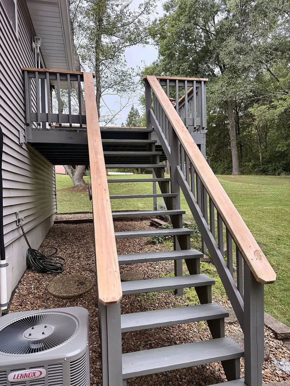 Deck stairs seen from the ground with new pressure-treated top caps on both stair rails and the deck railing