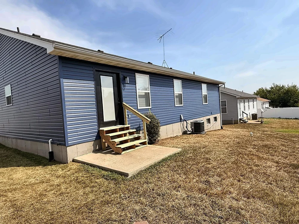 Back of the house with Midnight Blue siding, a new full-glass back door and new pressure-treated stairs on a concrete pad, with a new exterior light beside the door