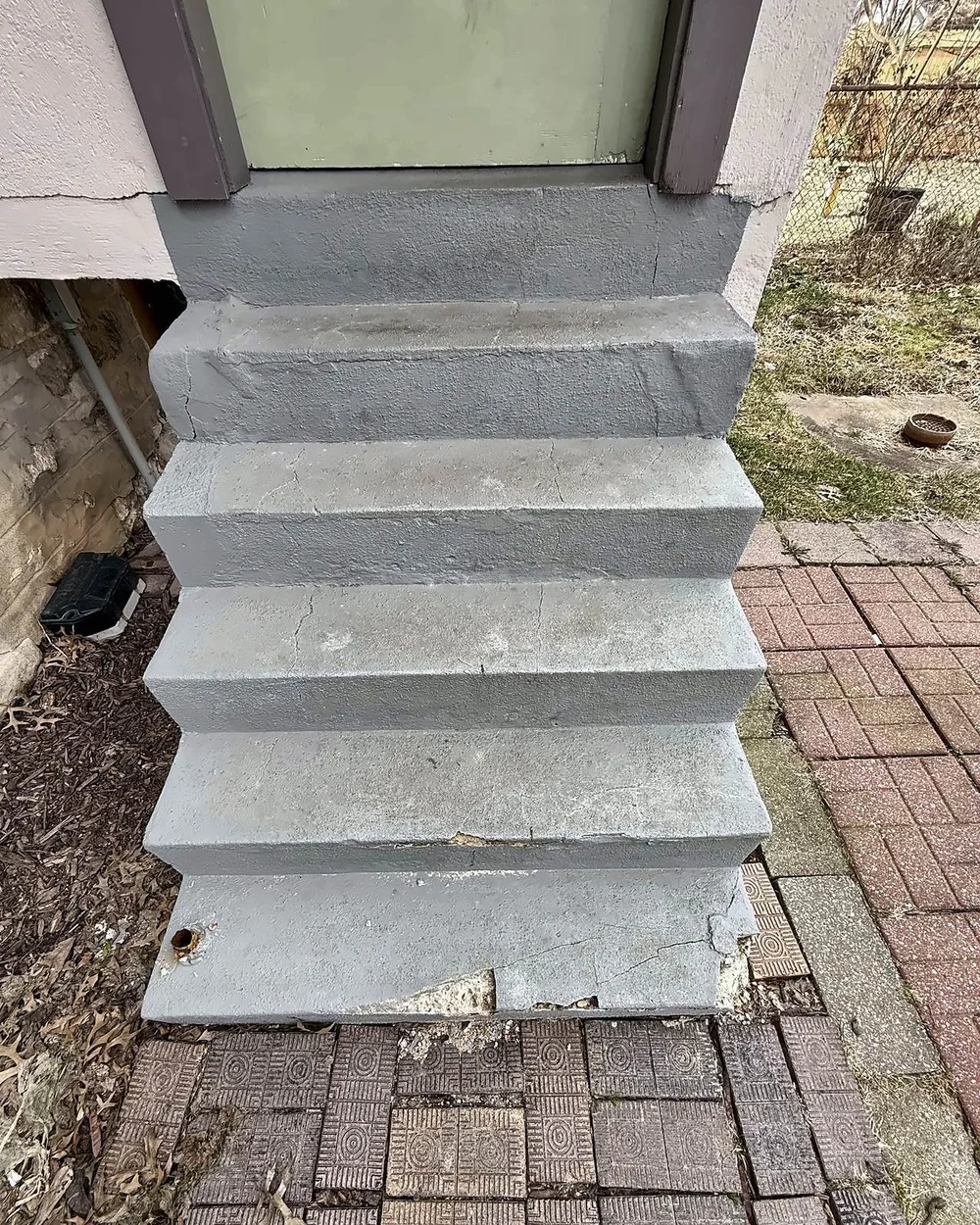 Old painted concrete back steps, cracked and crumbling at the bottom step, leading to a green back door