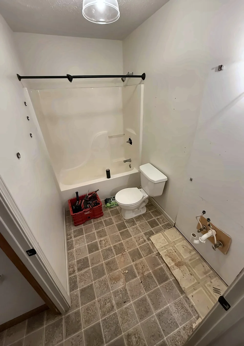 Hall bathroom before the remodel, with a one-piece fiberglass tub surround and a worn vinyl tile floor peeling up by the vanity wall