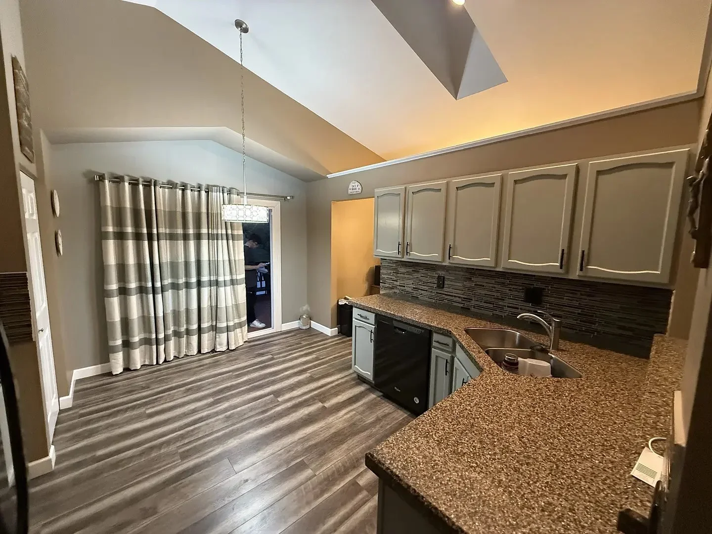 Modern kitchen with vaulted ceiling, granite countertops, gray cabinets, striped curtains, and wood flooring
