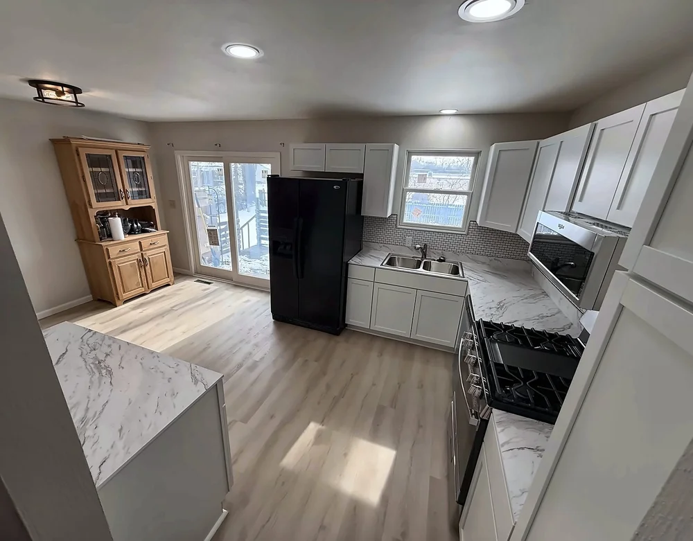 Finished kitchen sink wall and range wall with white shaker cabinets, marble-look counters and recessed lighting