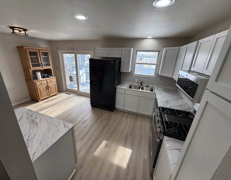 Finished kitchen sink wall and range wall with white shaker cabinets, marble-look counters and recessed lighting