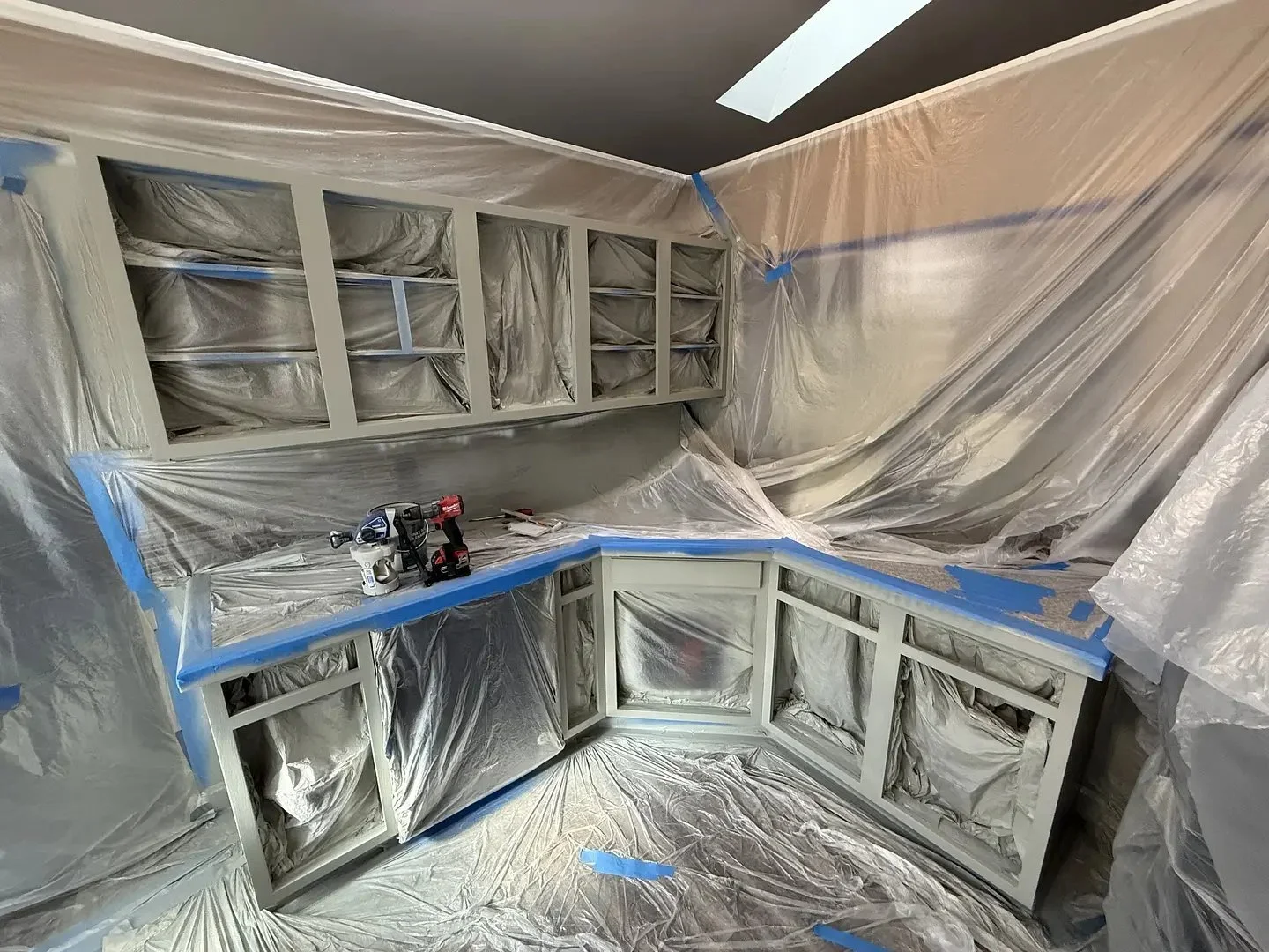 Kitchen cabinets covered in plastic sheeting with tools on the counter, preparing for painting or renovation