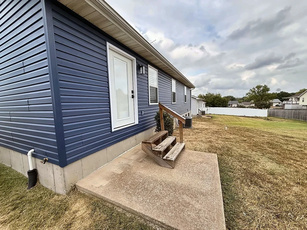 Back of the house in new Midnight Blue siding with the new door installed and the old wooden steps still in place