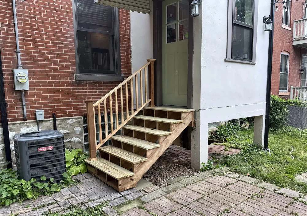 New pressure-treated wood back stairs with a wood handrail leading to a green back door on a brick and stucco home