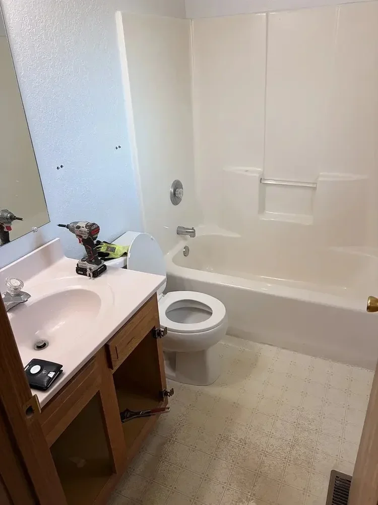 Bathroom under renovation with tools on the sink, an open cabinet, toilet, and bathtub
