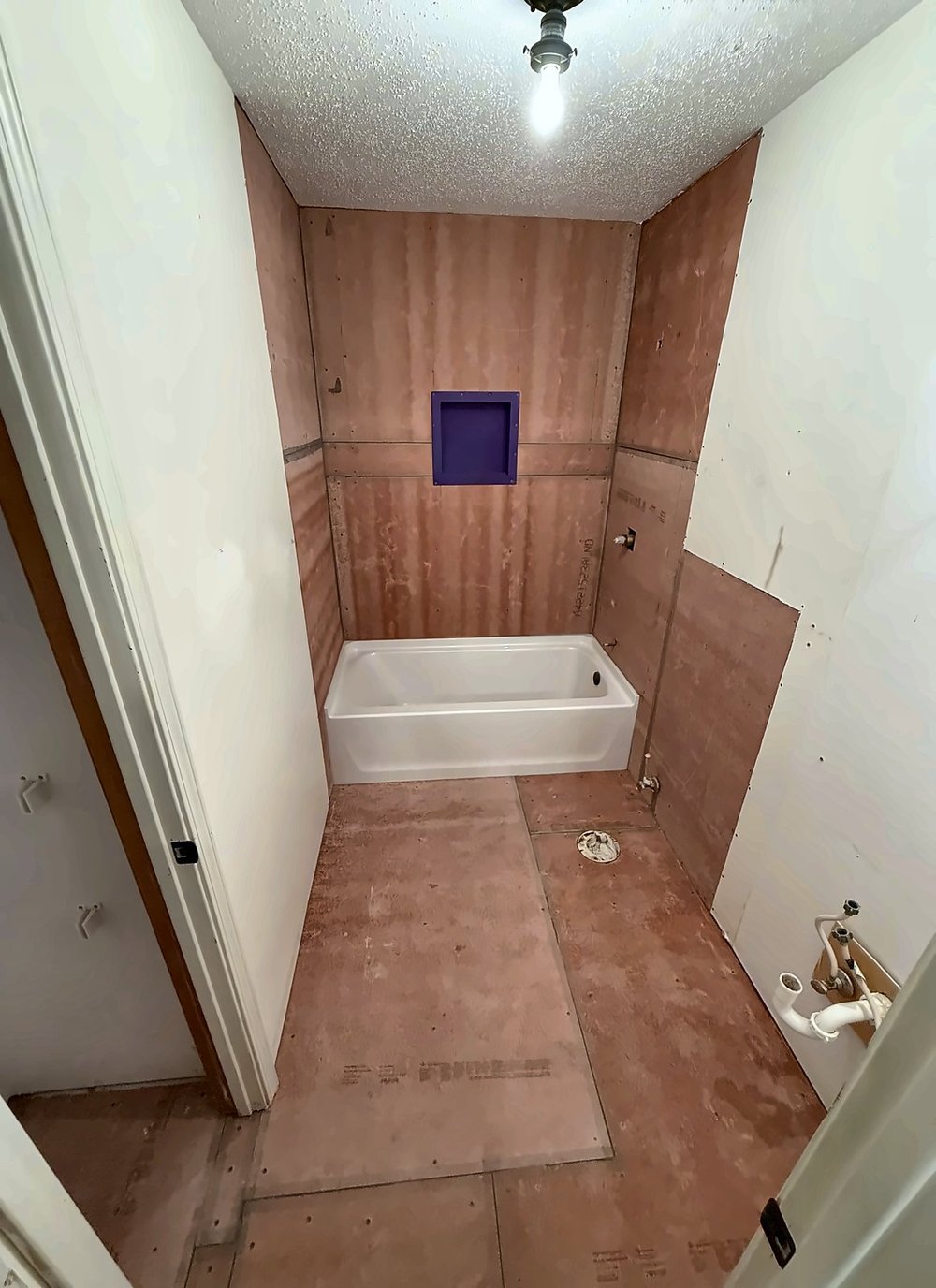 Bathroom during the remodel with cement board on the walls and floor, a new white tub, and a framed shower niche