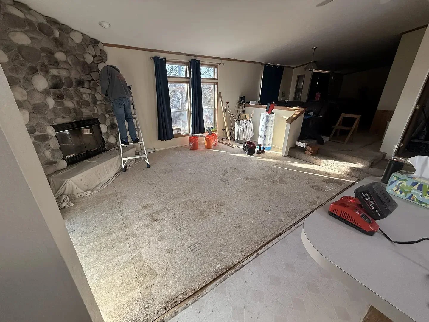 Living room under renovation, person on ladder working on stone fireplace