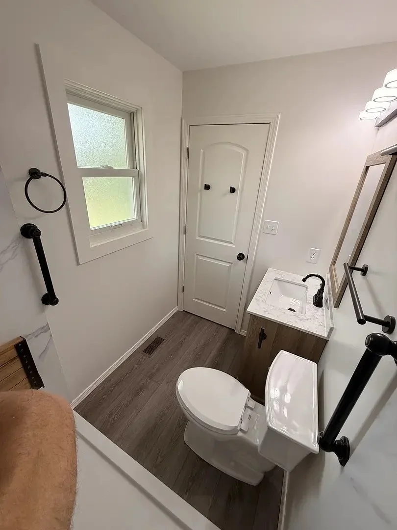 Small bathroom with a toilet, sink, and window. Light wood flooring and minimal decor