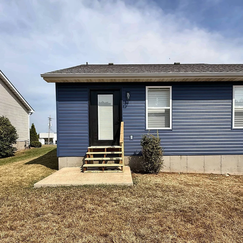 Straight-on view of the new black back door and pressure-treated stairs with a handrail against Midnight Blue siding