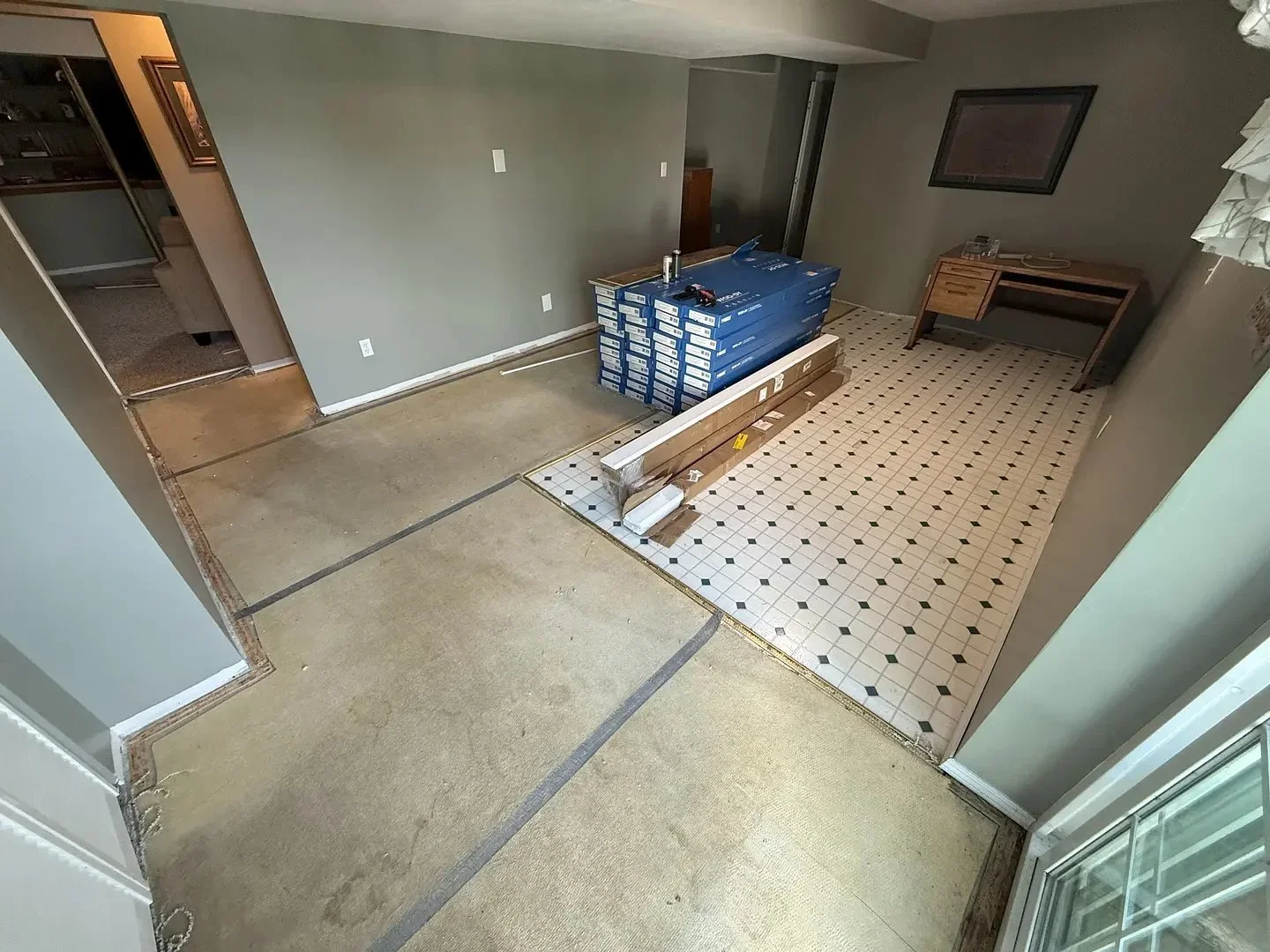 Room under renovation with bare floors, tiles, and stacked boxes. A small desk is in the tiled area