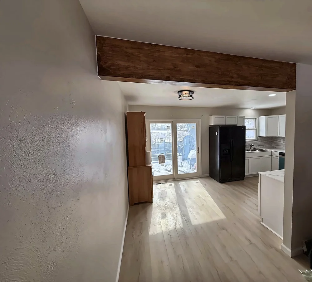View through the opening with a wood-wrapped beam into the remodeled kitchen and dining area