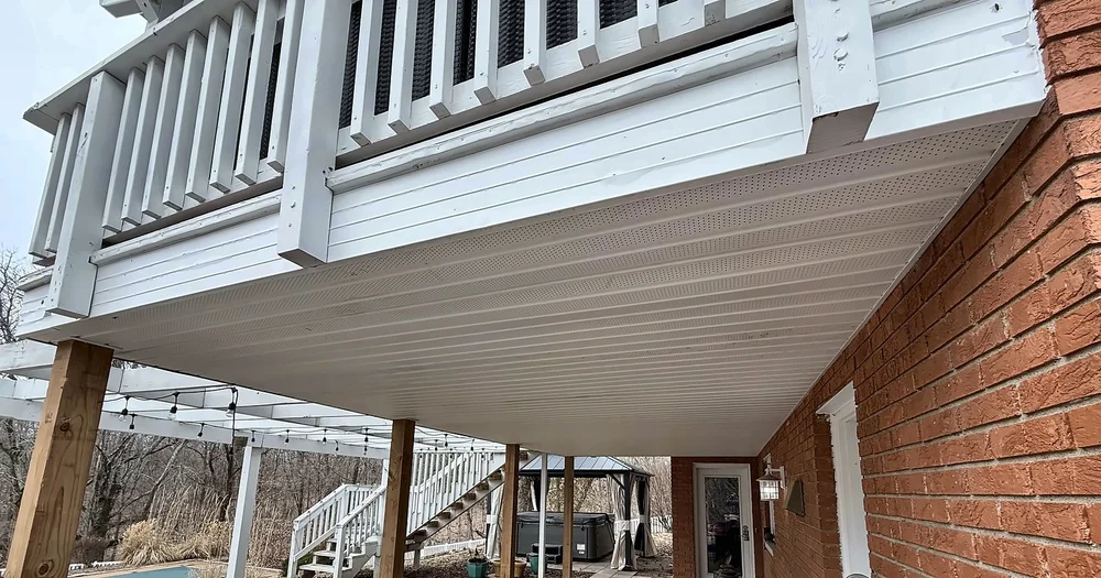 New white vented vinyl soffit installed under a second-story deck next to a brick walkout basement