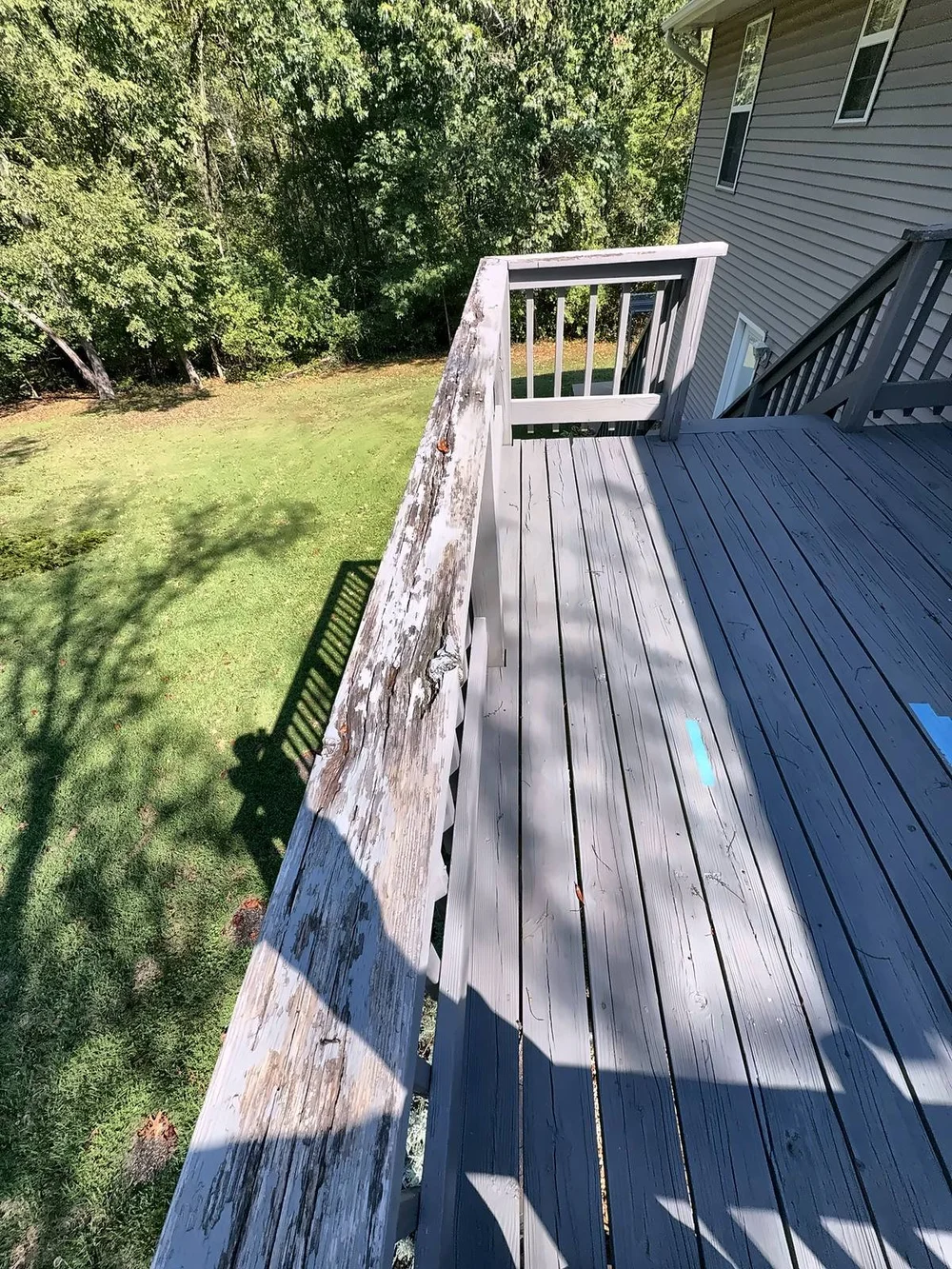 Old gray deck railing cap, weathered, peeling and cracked along its length
