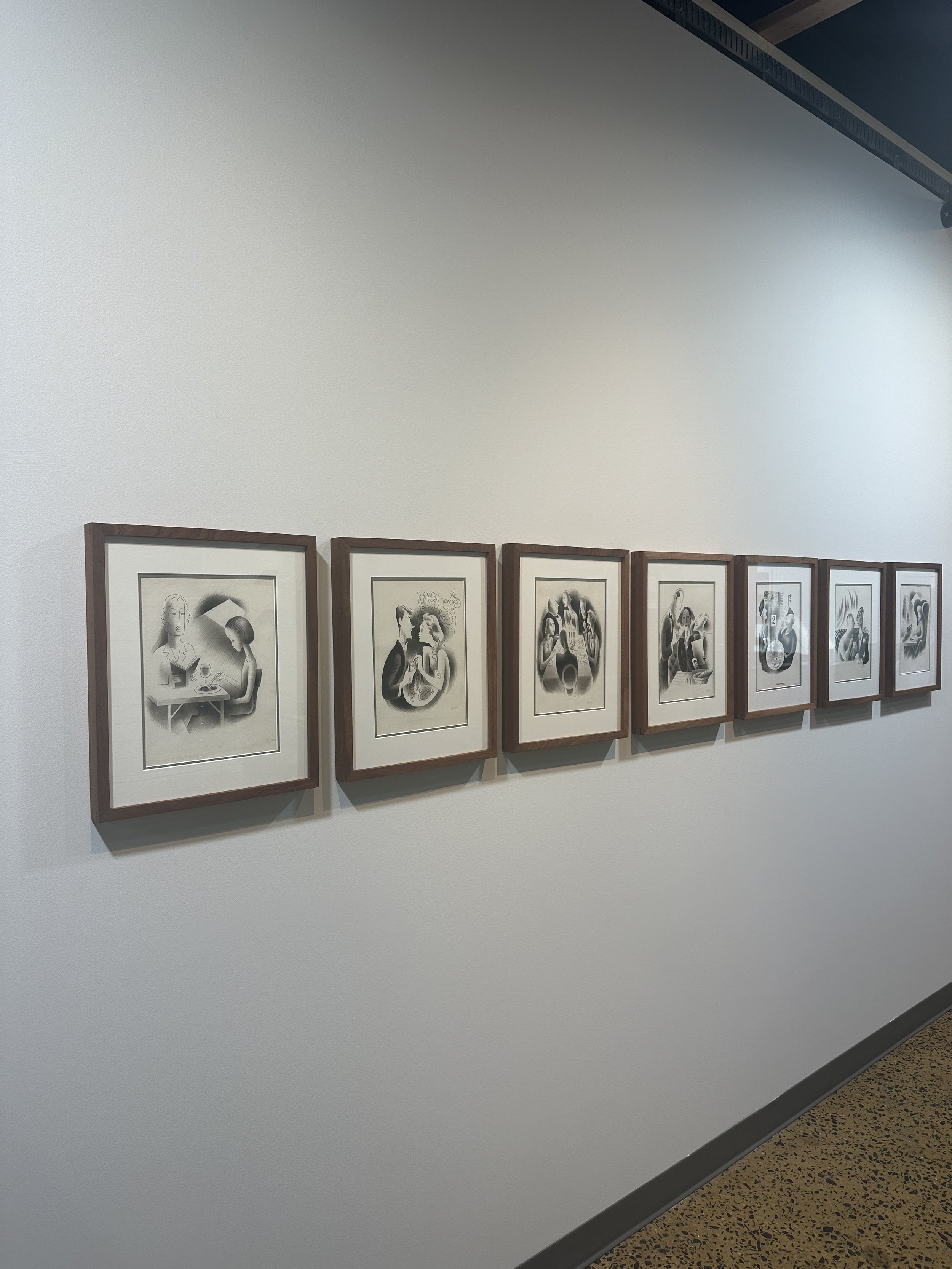 A series of framed black-and-white illustrations hung in a row on a white gallery wall.