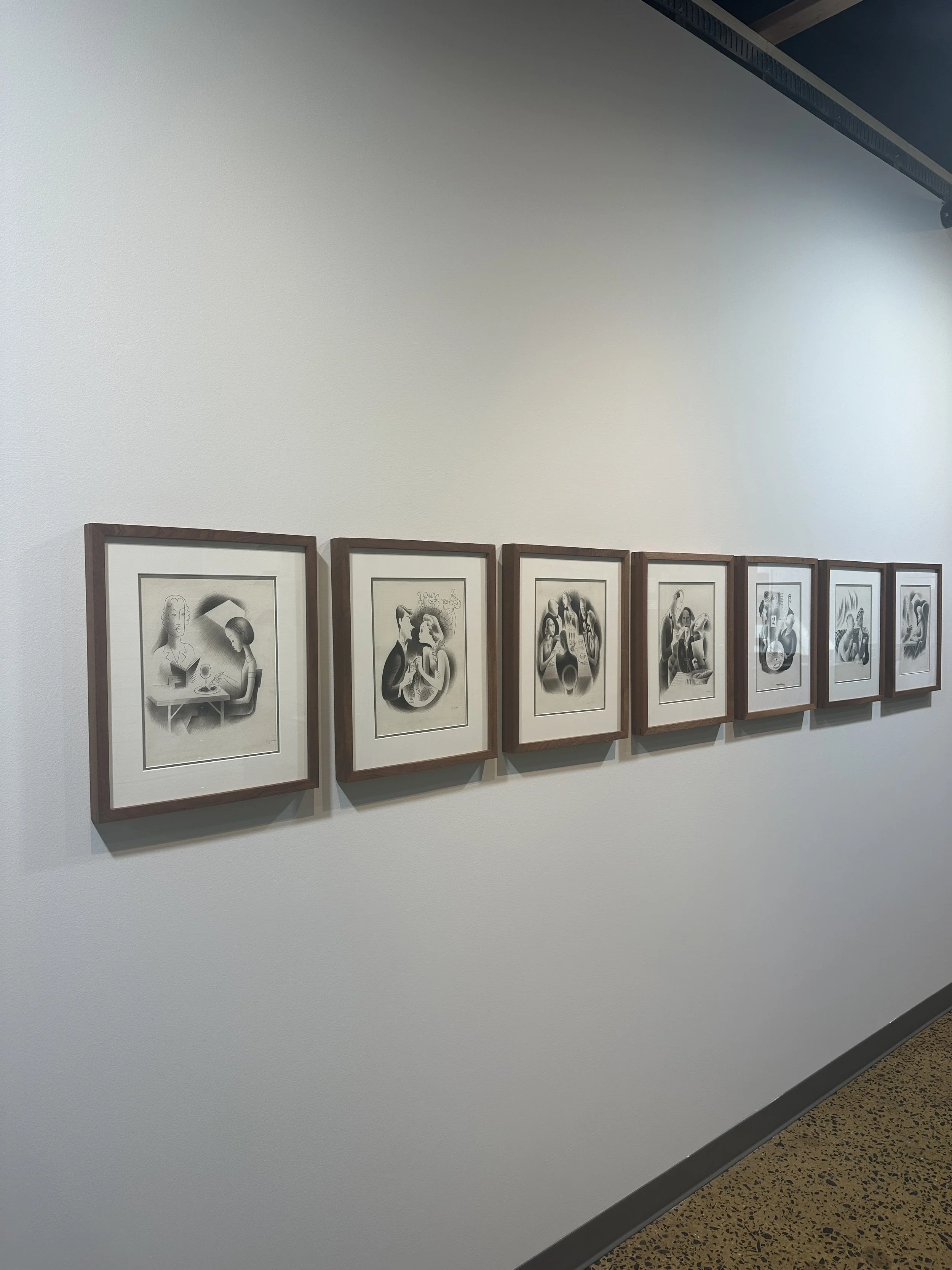 A series of framed black and white artwork depicting various romantic or intimate scenes, hung on a white gallery wall.