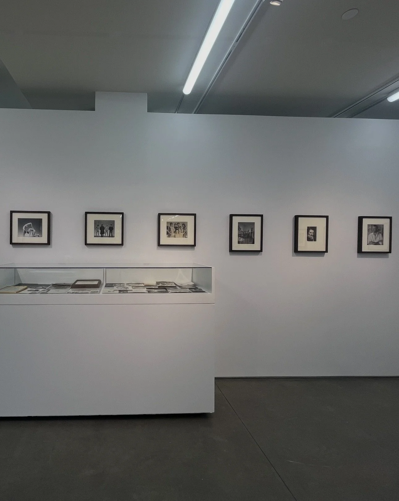 Gallery wall with framed black-and-white photographs and documents displayed in a museum or gallery setting.