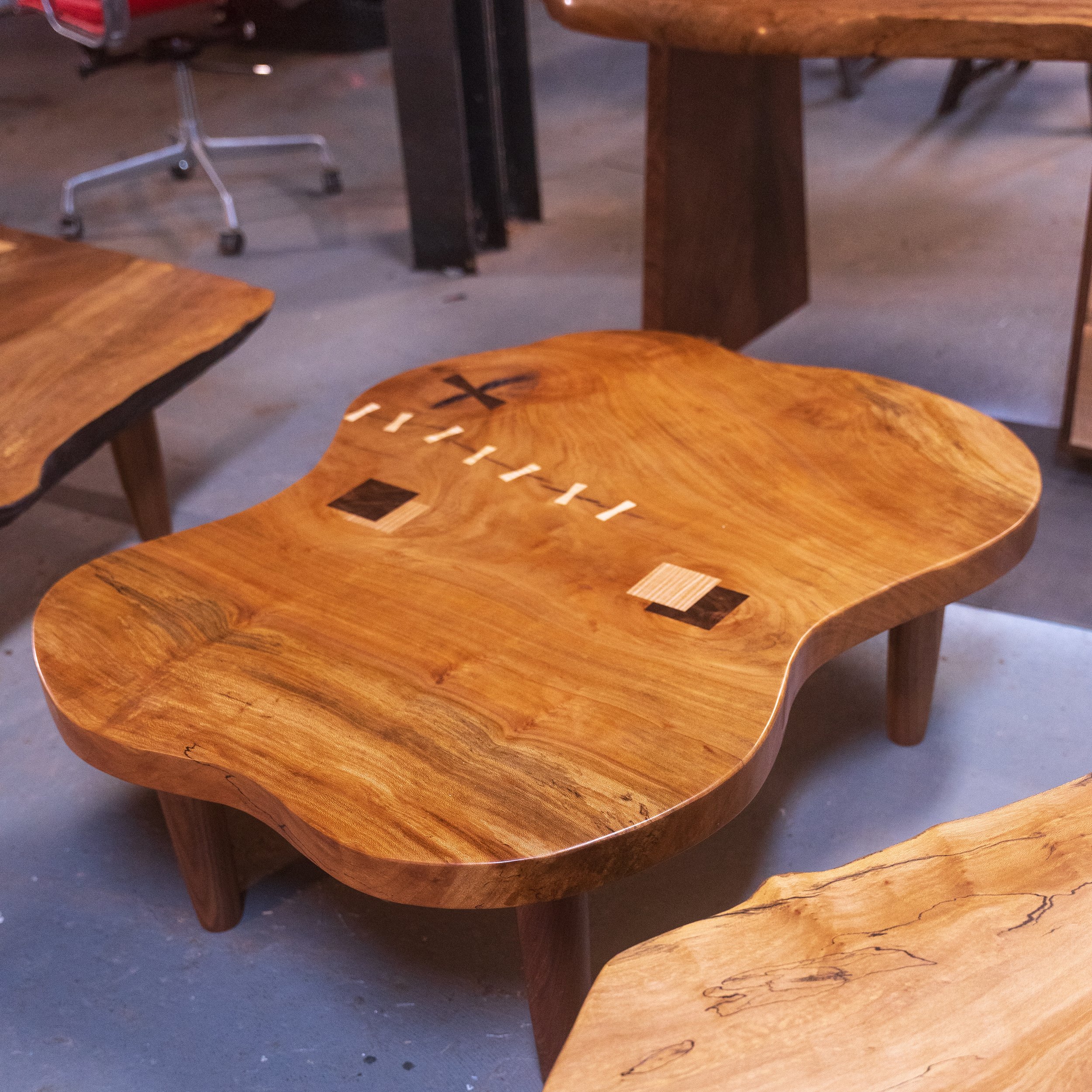 Close-up of wooden coffee tables with curved edges and black inlays, set against a concrete floor.