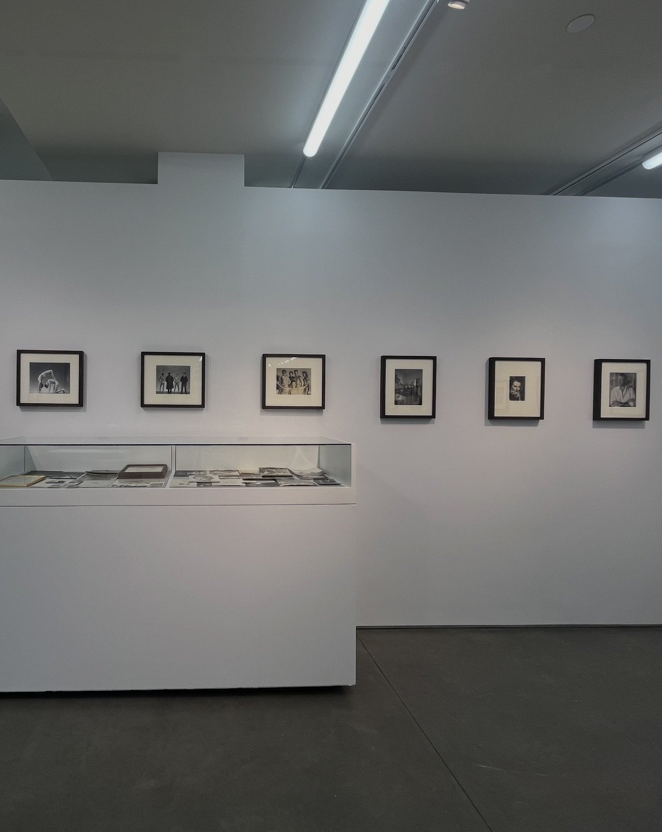 Gallery wall with six framed photographs and a glass display case with black and white photographs in an art museum.