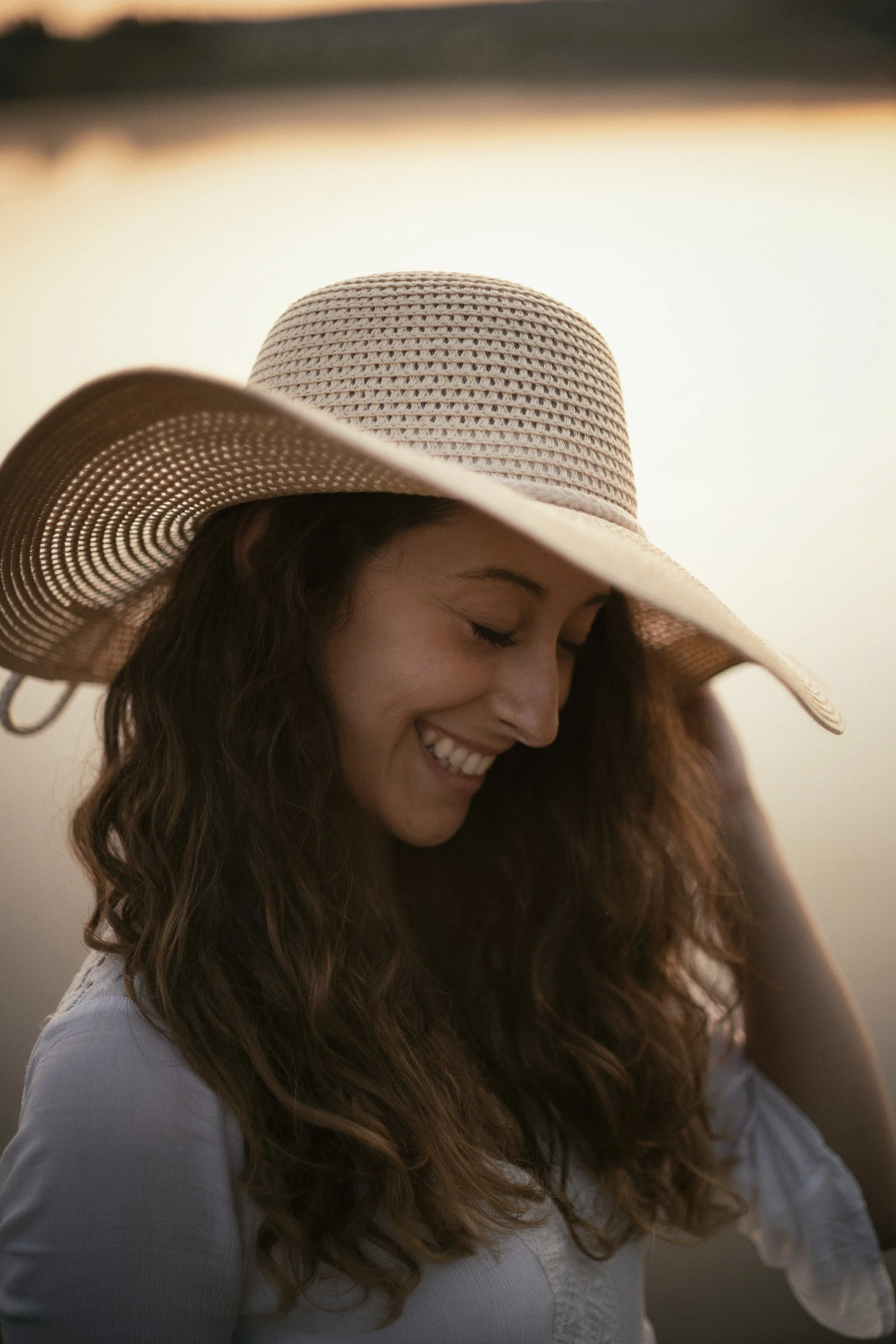 Portrait einer lachenden Frau mit langen Haaren und einem Strohhut an einem See
